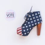 High heel with American flag design beside a voting sticker on white background.