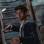 A man holding a gun in a dimly lit, mysterious urban setting.