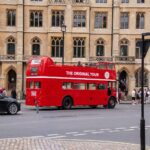 Vintage red double-decker bus offering tours in historic London with people nearby.