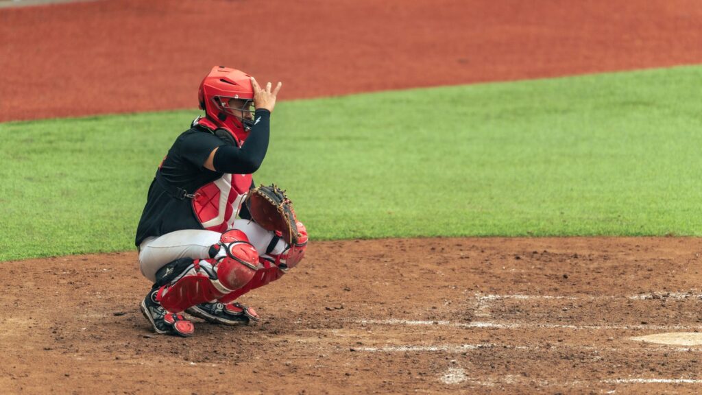 A baseball catcher in full gear giving a signal during a game.
