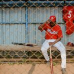 Athlete in uniform seated in a dugout bench holding a baseball bat.