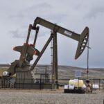 Oil pump jack and equipment at remote industrial site under cloudy sky.