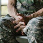 A soldier in camouflage uniform rests with hands folded, depicting calmness.