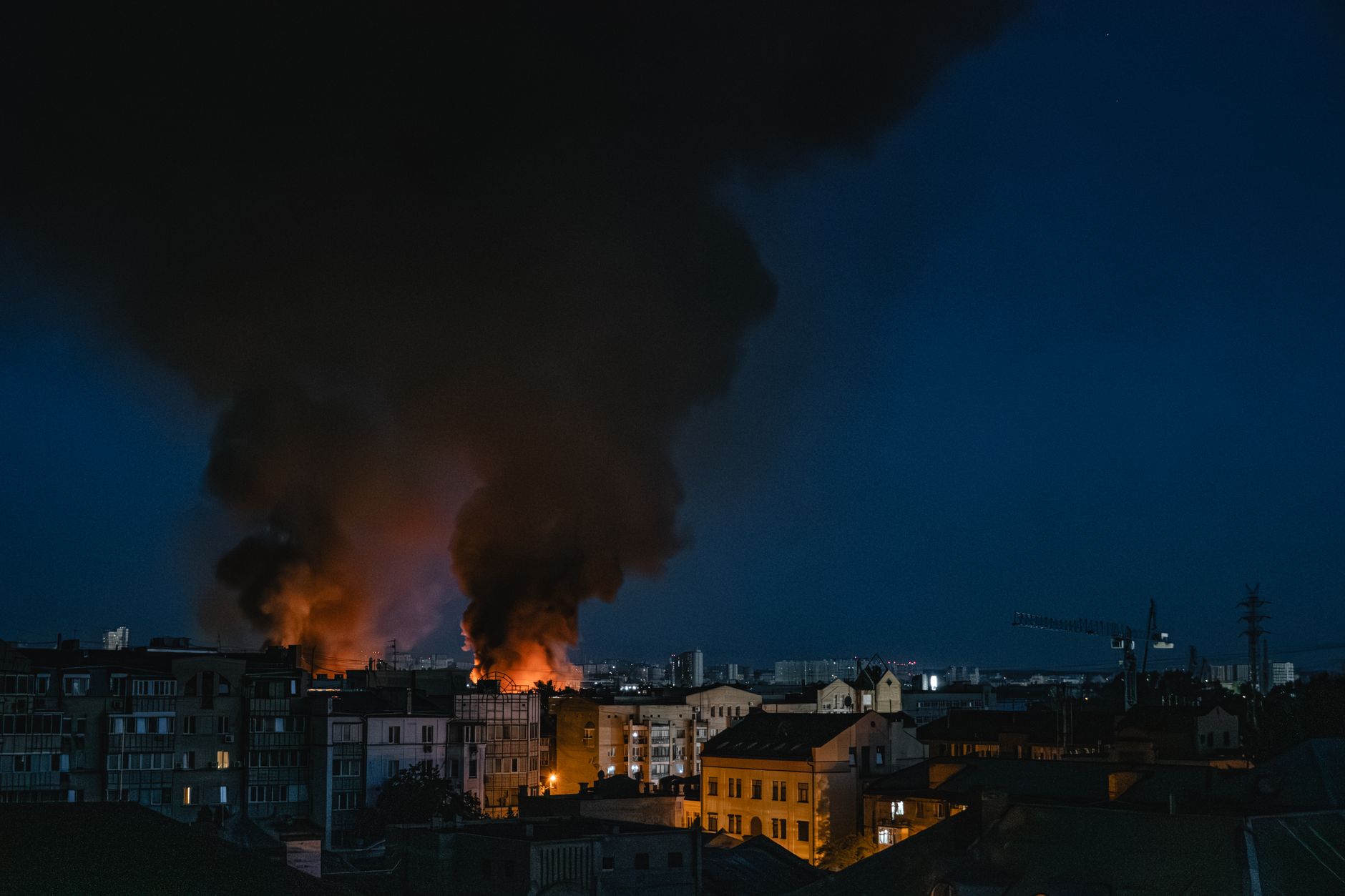 A dramatic scene of a fire with smoke rising over the cityscape of Kyiv at night.