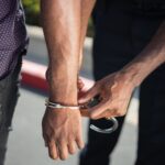 Close-up of a police officer handcuffing a suspect outdoors, enforcing law.