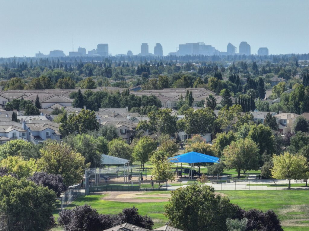 Aerial view of Sacramento suburb with skyline in the distance, showcasing residential and urban contrast.