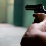 Close-up shot of hands aiming a pistol in an indoor shooting range, emphasizing focus and tension.