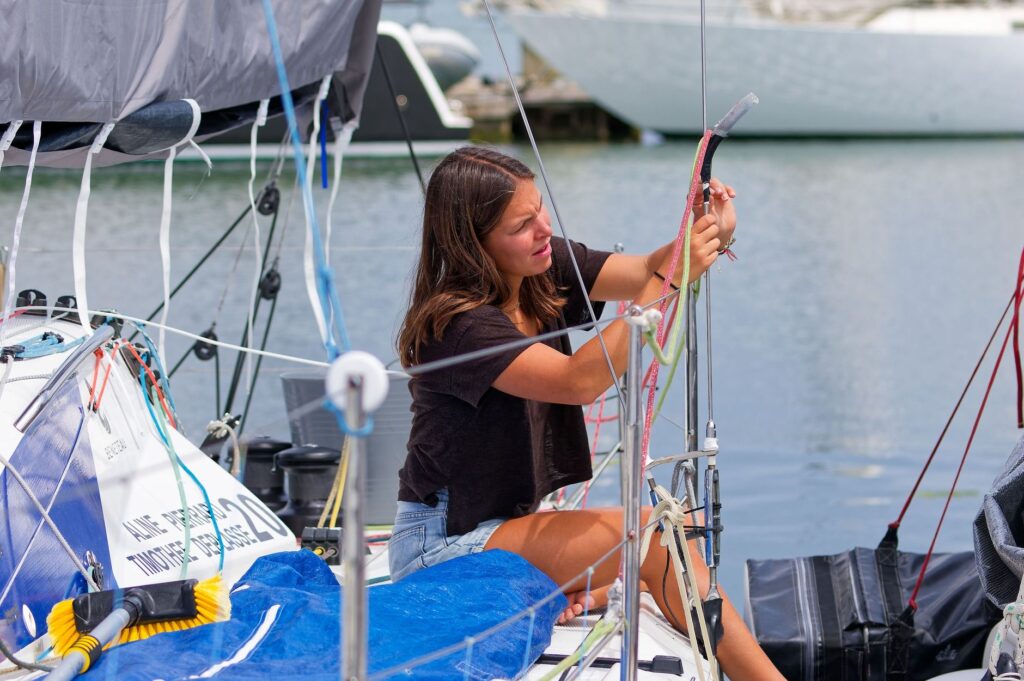 A young woman adjusts a sail on a docked sailboat, showcasing her sailing skills.