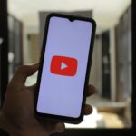 Close-up of a hand holding a smartphone displaying the YouTube logo in a well-lit room.