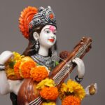Close-up of a Saraswati statue adorned with vibrant marigold flowers, symbolizing wisdom and art.