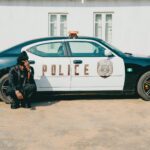 Police officer seated by car in urban area during the day.