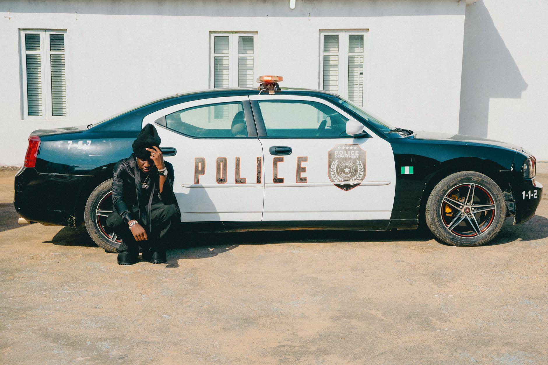 Police officer seated by car in urban area during the day.