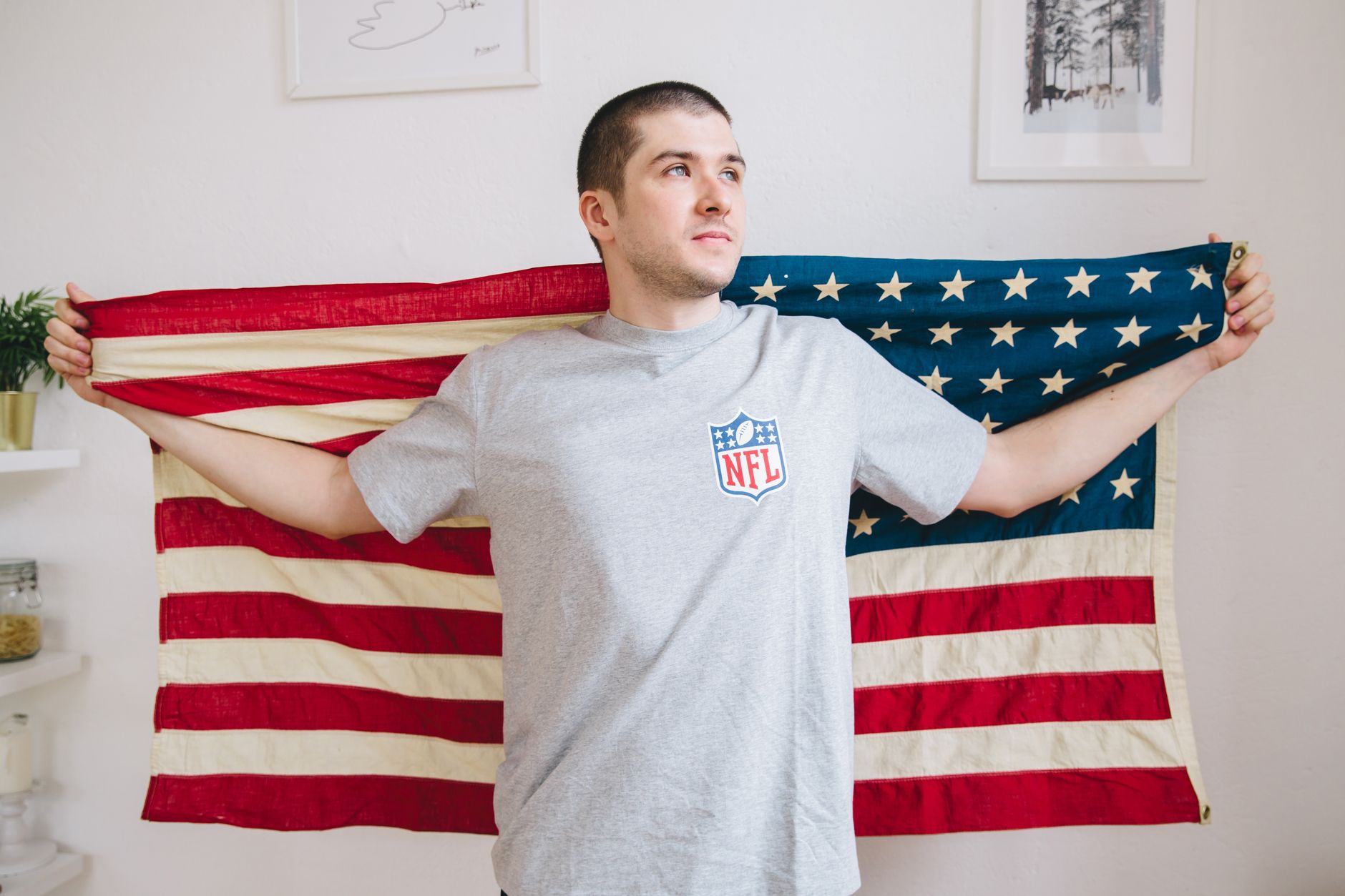 Man holds American flag indoors, expressing patriotism with casual NFL shirt.