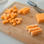 Close-up of cheddar and colby-jack cheese slices on a wooden cutting board with a knife.