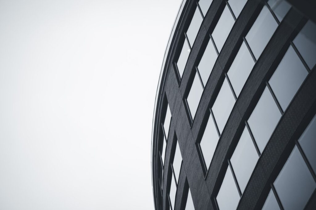 Low-angle view of a modern curved building with glass windows in grayscale.