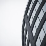 Low-angle view of a modern curved building with glass windows in grayscale.