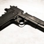 Close-up of a black metal handgun on a light surface, showcasing firearm details.