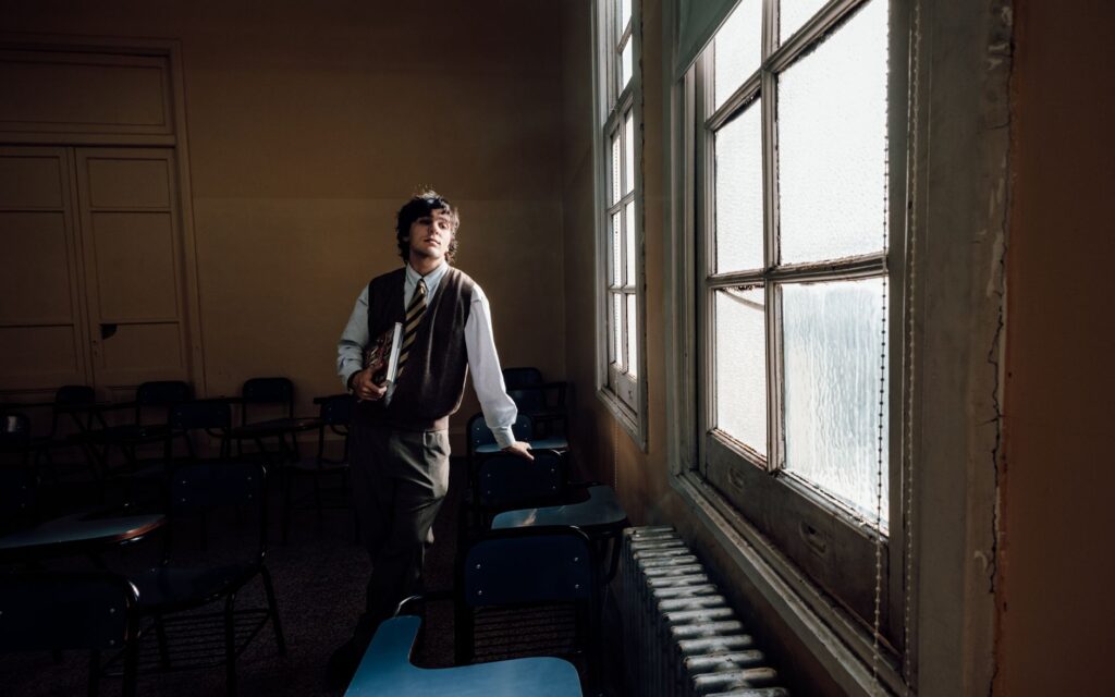 A thoughtful student gazes through a sunlit window in a Buenos Aires classroom.