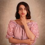 A beautiful woman poses confidently in a pink dress against a textured background.