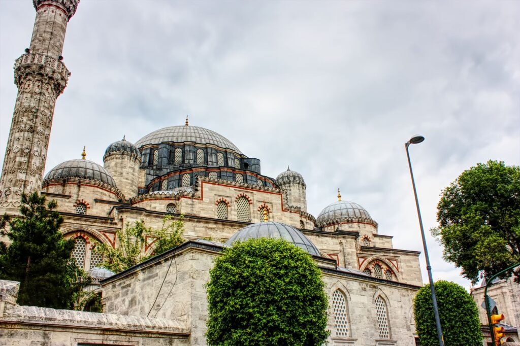 A detailed view of Shehzade Mosque's domes and minaret in Istanbul under an overcast sky.