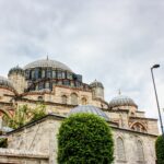 A detailed view of Shehzade Mosque's domes and minaret in Istanbul under an overcast sky.