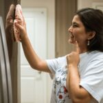 A woman cheerfully wipes a refrigerator, showcasing a moment of home cleaning.