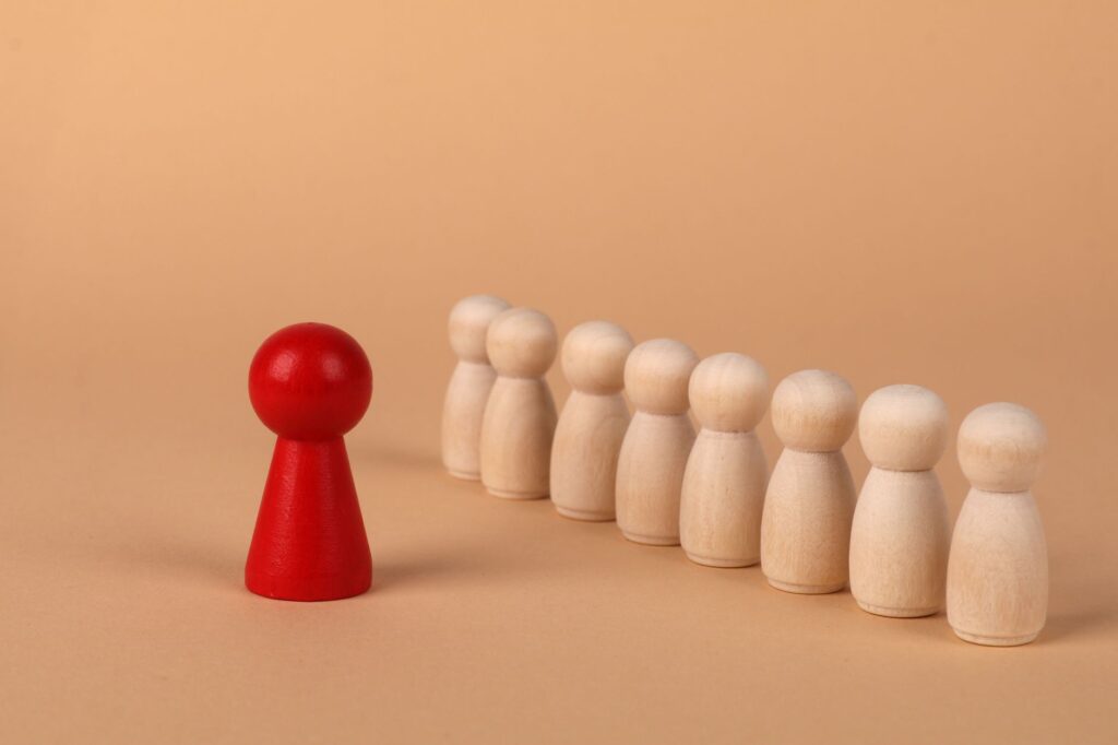 A red pawn stands out as it leads a group of wooden pawns on a beige background symbolizing leadership.