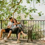 A couple embraces on a park bench under a tree, capturing a serene and romantic moment.