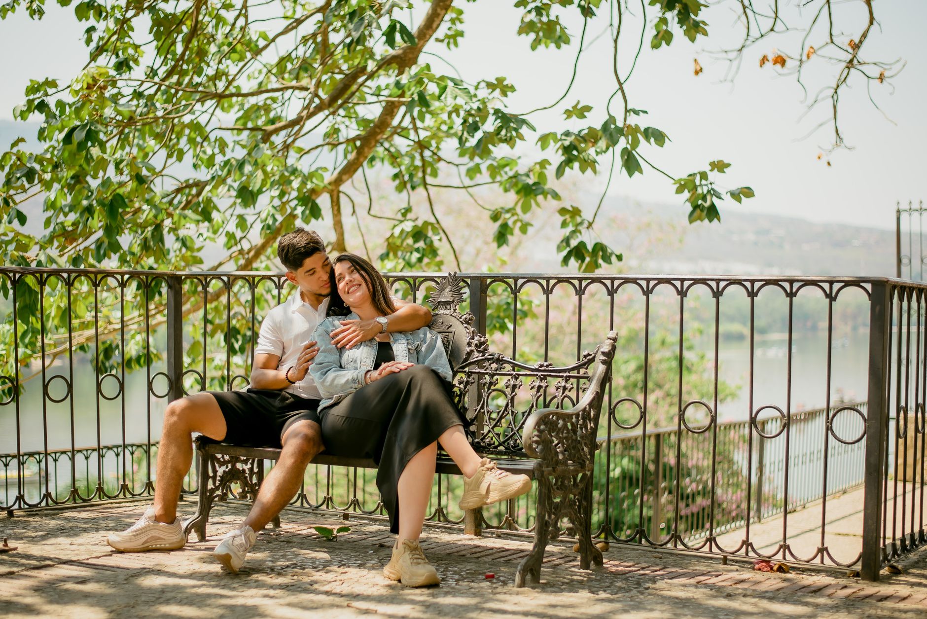 A couple embraces on a park bench under a tree, capturing a serene and romantic moment.