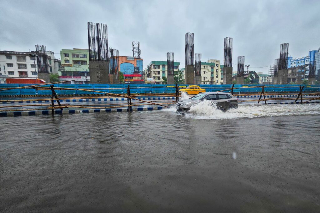 A car navigates through a flooded street in Kolkata, India during monsoon season.