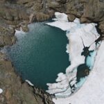 Explore the striking aerial view of a frozen glacier lake in Binn, Switzerland, surrounded by rugged rock formations.