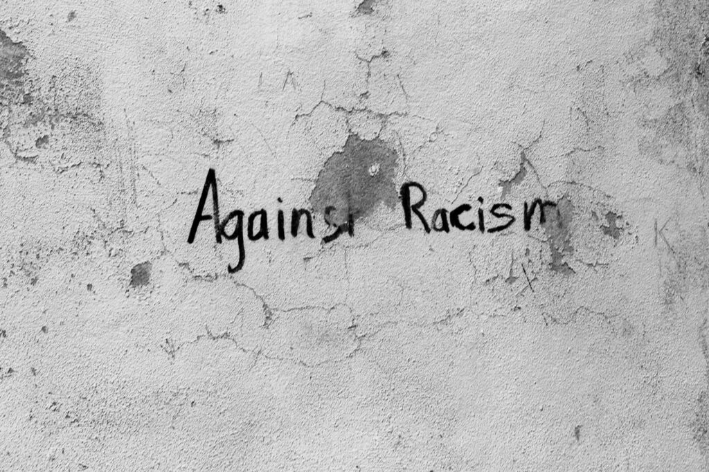 Black and white graffiti on a cracked wall with the message 'Against Racism' in Guarda District, Portugal.