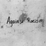 Black and white graffiti on a cracked wall with the message 'Against Racism' in Guarda District, Portugal.