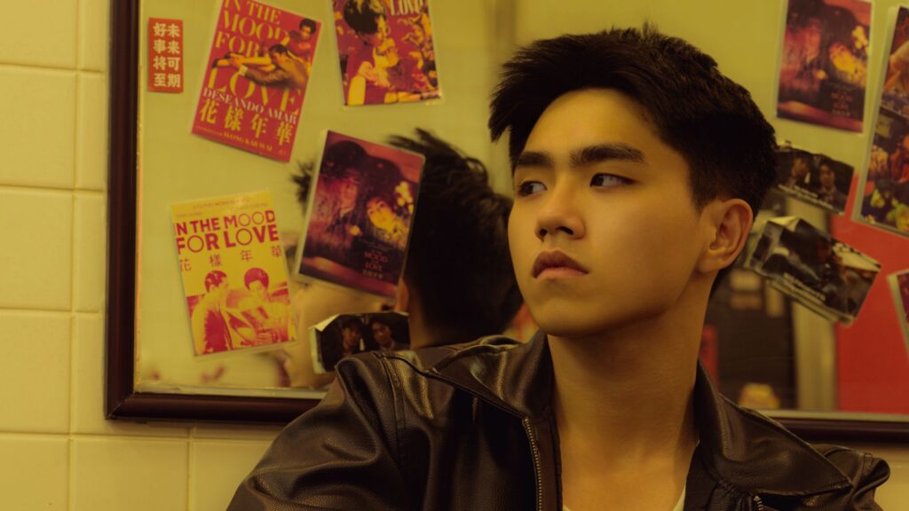 Young man in leather jacket pondering near reflective mirror with film posters.