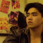 Young man in leather jacket pondering near reflective mirror with film posters.