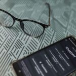 Eyeglasses next to a smartphone displaying the ChatGPT AI app on a patterned surface.
