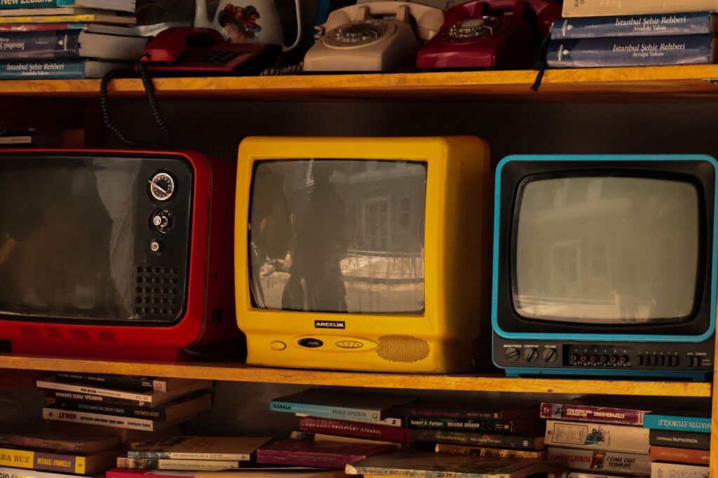 A collection of vintage retro TVs and old telephones on a wooden shelf, evoking nostalgia.