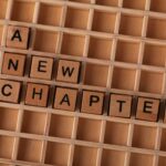Scrabble tiles spelling 'A New Chapter' on wooden grid, symbolizing new beginnings.