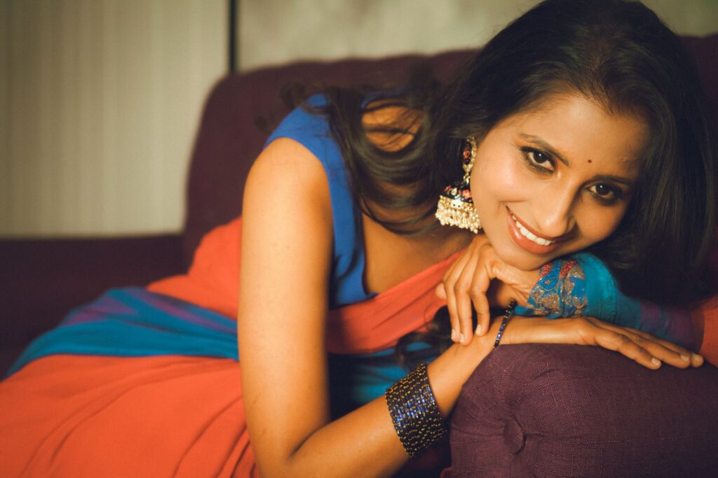 Portrait of a smiling woman in colorful traditional attire relaxing on a sofa indoors.
