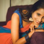 Portrait of a smiling woman in colorful traditional attire relaxing on a sofa indoors.