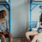 Two women chatting and smiling in a hostel room with bunk beds.