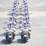 A line of South Korean police officers on motorcycles holding flags in an urban parade.