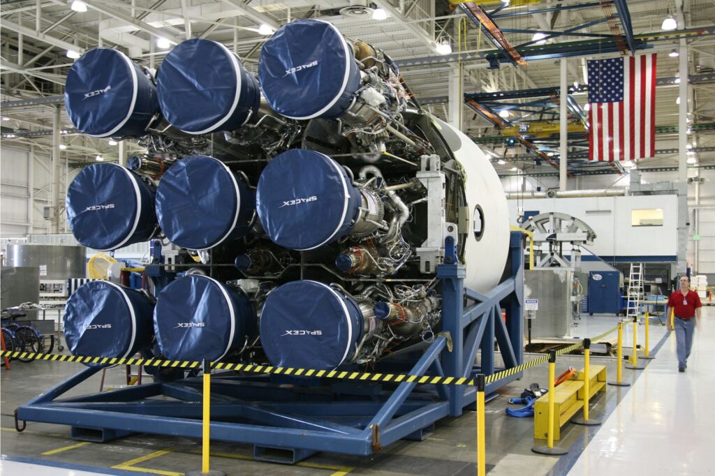 Unfinished details of rocket engines under construction placed on metal platform during assembly at space factory with hanging US flag on background