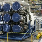 Unfinished details of rocket engines under construction placed on metal platform during assembly at space factory with hanging US flag on background