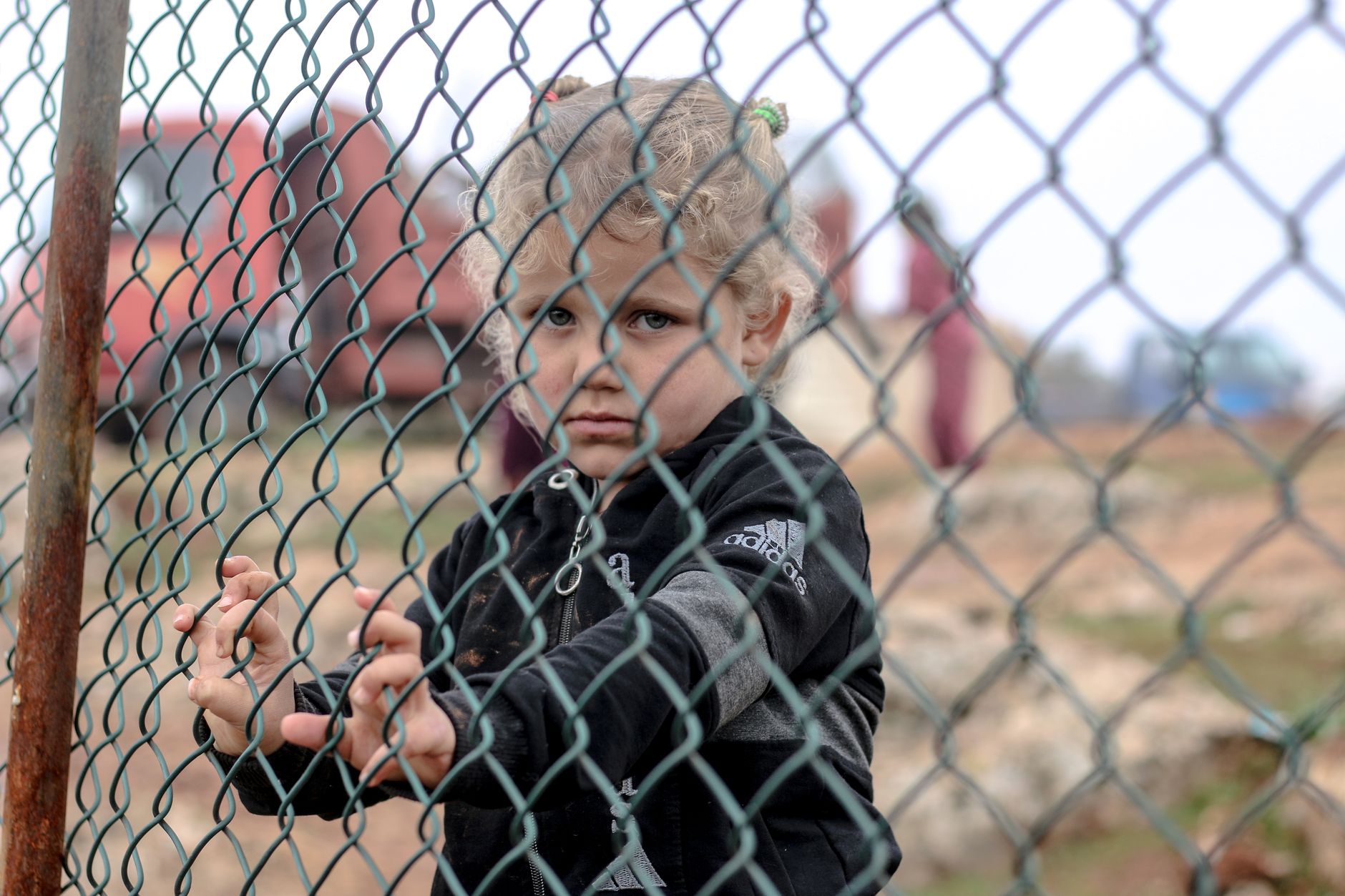 Sad ethnic child standing near metal net against freight car and looking at camera