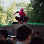 Spider-Man cosplayer posing for photos at an outdoor event, attracting a lively crowd.