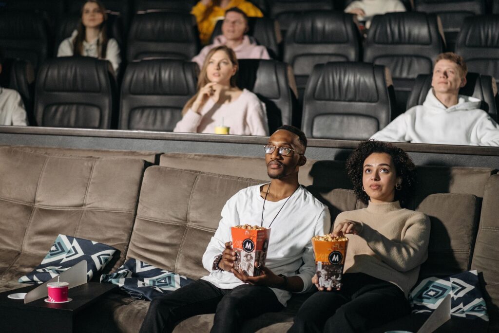 A couple enjoys popcorn while watching a movie in a cozy cinema environment, surrounded by others.