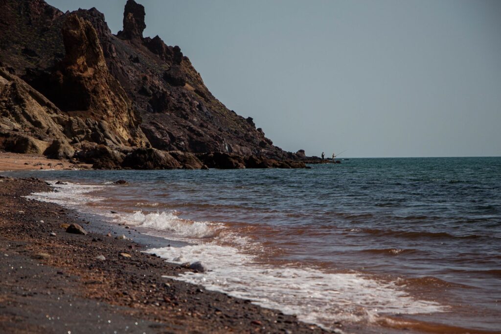 Waves crash on the rocky shore of Hormoz Island, Iran with clear blue skies.