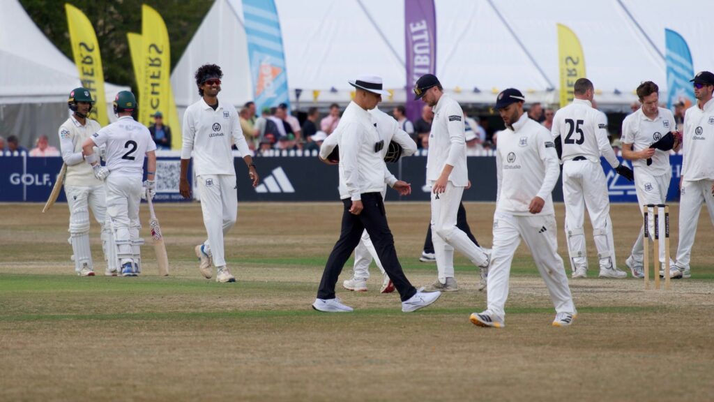 Cricket players and umpire on field during a match in Cheltenham, England.