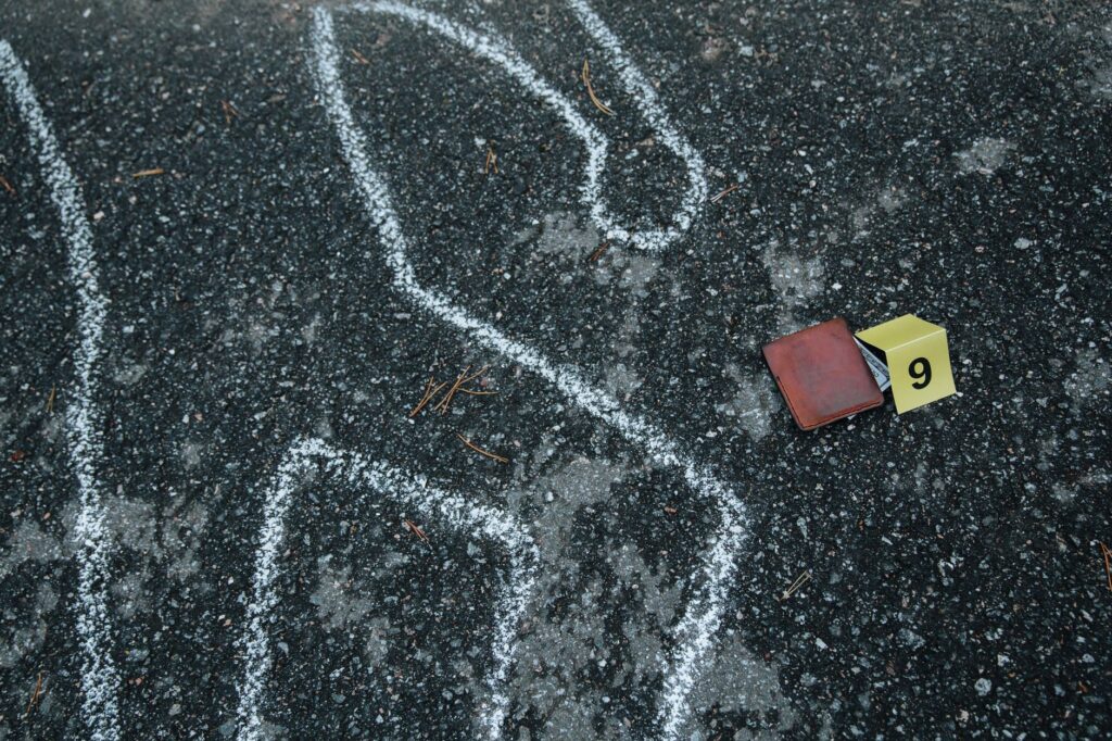 Crime scene with a chalk outline and evidence marker on asphalt.